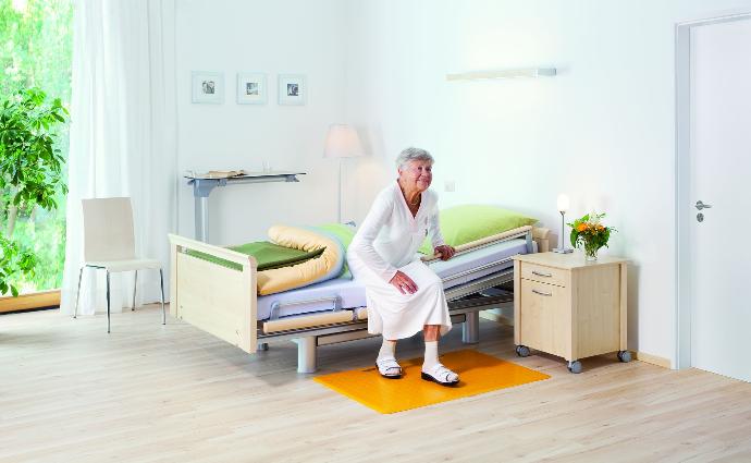 Seniorin steht auf eine Bodenmatte in einem Pflegezimmer