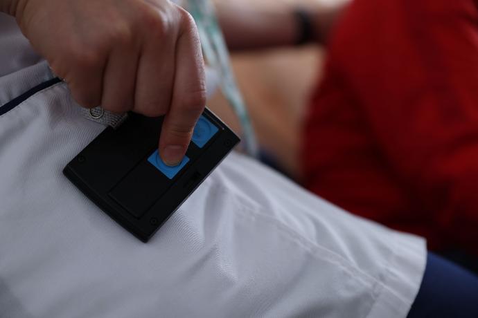 SmartLiberty Personalbadge von hinten mit Finger auf Knopf für Assistenzruf