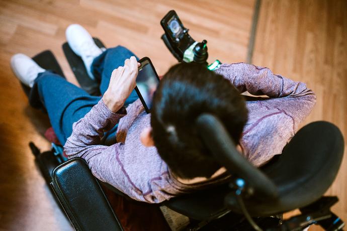 Mann im rollstuhl von oben abgebildet mit Smartphone in der Hand
